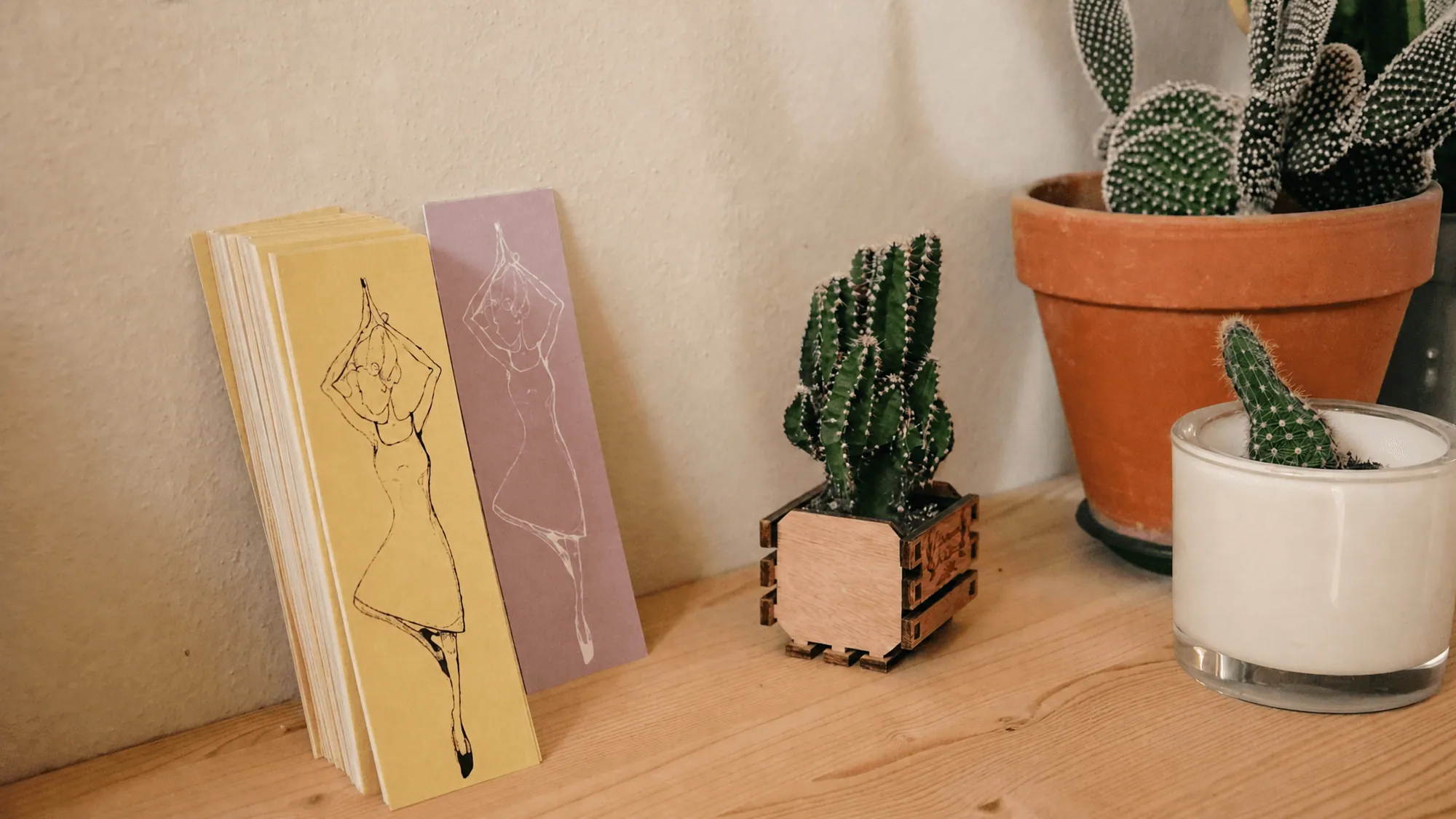 Dettaglio dello studio · segnalibri illustrati, cactus e candela su mensola di legno